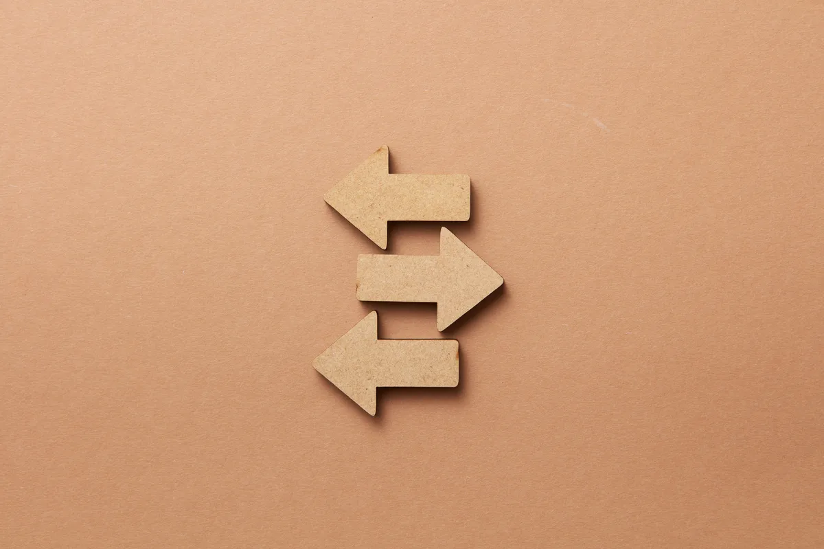 Close-up of three wooden arrows pointing in opposite directions on a beige surface.